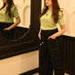 Woman in a green top and black pants standing in front of a mirror.