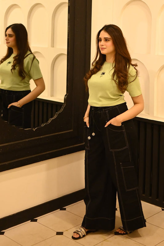 Woman in a green top and black pants standing in front of a mirror.